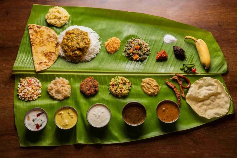 A traditional Andhra banana-leaf meal laid out on a wooden table, with rice, curries, chutneys, vegetable sides, papad, dal, sweets and a banana.