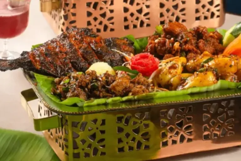 An Andhra non-veg platter in an ornate brass basket lined with banana leaf, holding grilled fish, fried meat pieces and prawns with garnish.